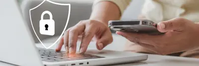 A person is using a smartphone and typing on a laptop. There is a digital lock icon, symbolizing security, near the devices.