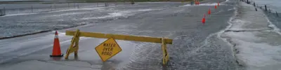 Waterfront path blocked by cones and caution barrier sign.
