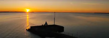 Sunset over calm water with pier silhouette and golden reflection on horizon