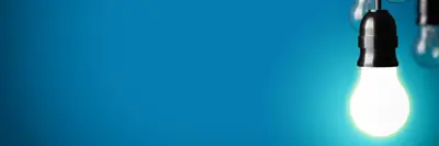 A brightly lit bulb hanging against a solid blue background, partially revealing other unlit bulbs in the right corner.