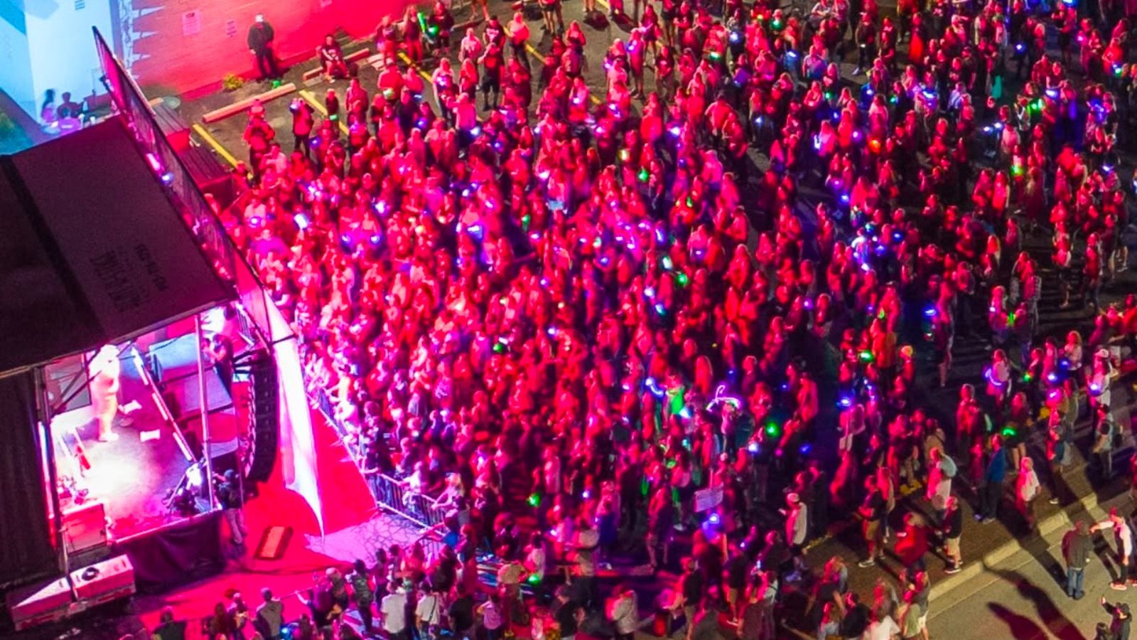 Large crowd standing by stage of live music performance shaded in bright pink lighting