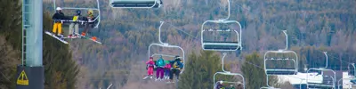 Chairlifts carrying skiers above a forested hillside in a ski resort setting