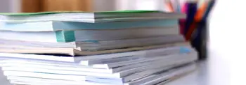 Stack of books or documents on a desk with blurred office supplies in background