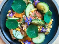Aerial image of a bowl full of salad and garnished with edible purple flowers 