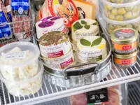 Image of the inside of a fridge at a gourmet food shop full of cheese, charcuterie, and olives 