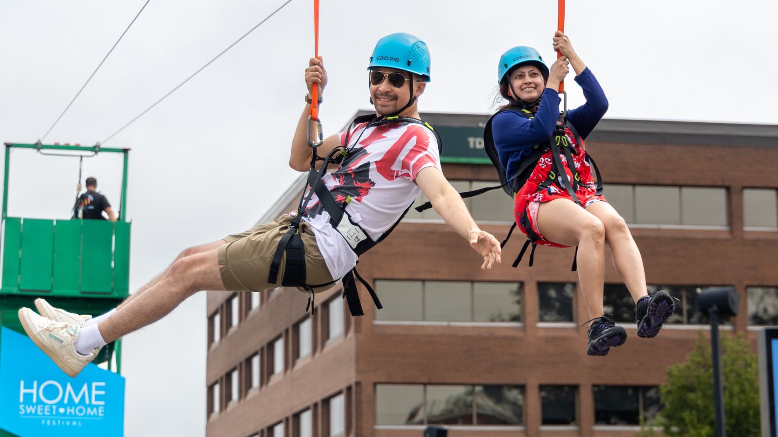 Two people smiling on zipline with brown building in the back