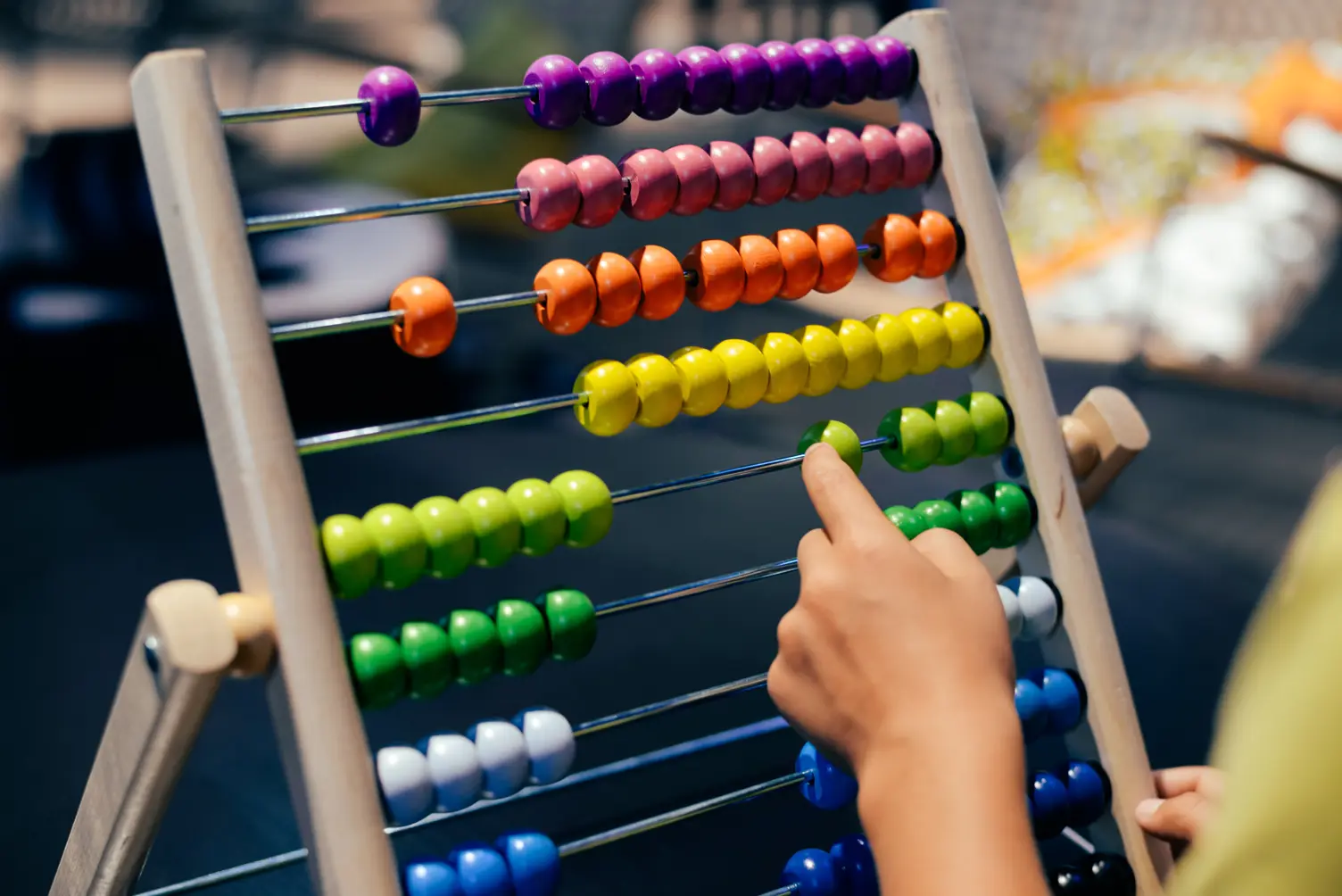 A person using an abacus with rows of colorful beads, including green, blue, and white, on a wooden frame.