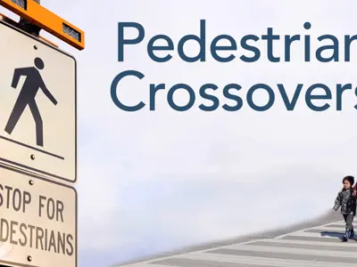 Image shows a mother and son walking across a pedestrian crossover painted on the road with thick white stripes, along with a road sign that says “Stop for pedestrians” and text over the image that states “Pedestrian Crossovers.”