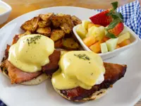 Eggs benedict topped with rich hollandaise, home fries, and fresh fruit. 